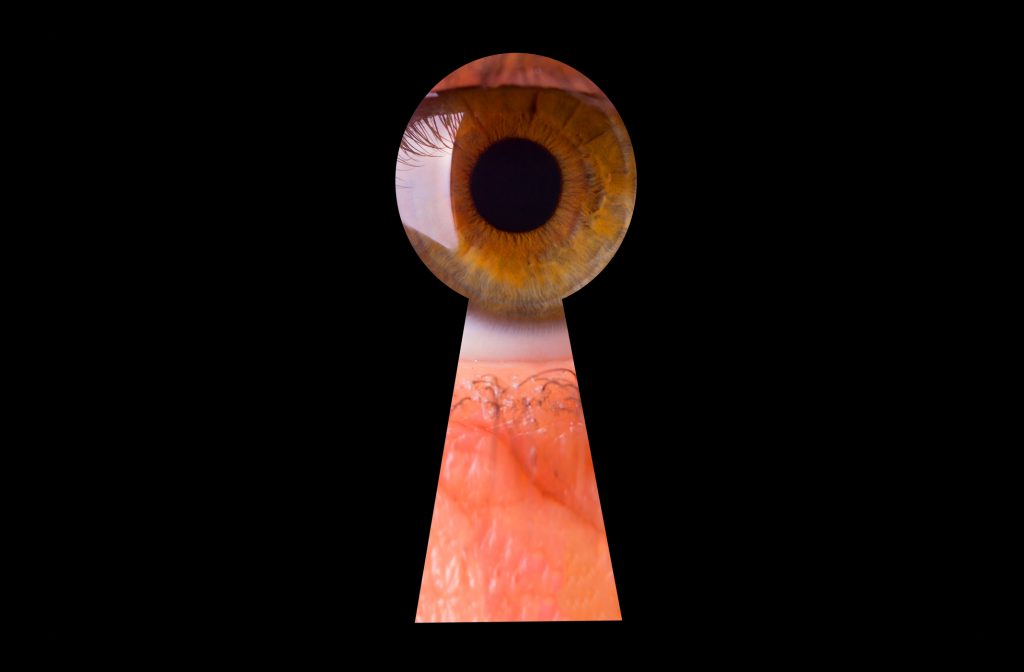 Female eye peeking through a keyhole concept for curiosity, stalker, surveillance and security