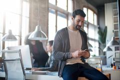 homme-assis-sur-le-coin-de-son-bureau-regarde-son-smartphone