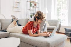 jeune femme regarde son ordinateur allongée sur son canapé