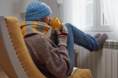 Un monsieur bien emmitouflé près de son radiateur, dans son salon. 