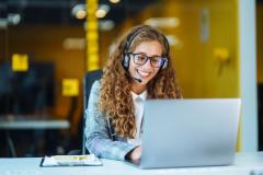 Femme souriante au travail avec un ordinateur et un casque.