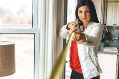 Femme mesurant une maison avec un mètre jaune.