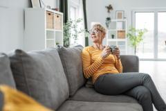 Femme buvant son café dans le salon, sur son canapé gris.