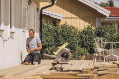 Un homme est en pleine construction d'une terrasse en bois, accolée à sa maison
