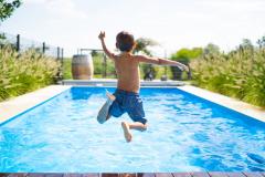 Un jeune garçon en maillot de bain saute dans une belle piscine privative bordée de plantes