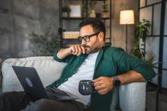 Homme assis sur son canapé, avec son mug et son ordinateur.