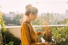Une jeune femme portant ses cheveux relevés en chignon s'occupe de ses plantes vertes sur son balcon