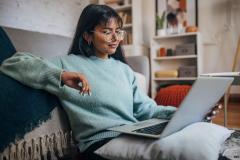 jeune femme assise près de son canapé regarde son ordinateur