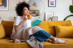 Femme afro américaine souriante, avec un mug sur son canapé jaune moutarde. 