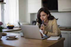Femme avec marinière jaune et blanche recherchant une information sur son ordinateur, dans la cuisine. 
