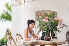 Femme recherche des conseils pour vendre sa maison l'été depuis son ordinateur sur sa terrasse