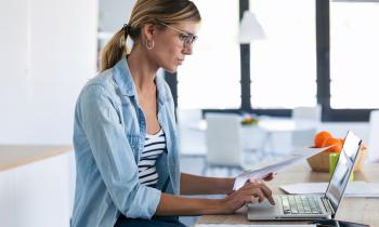 femme sur ordinateur tenant une feuille dans sa main