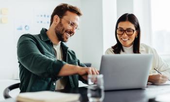 Une femme et un homme devant un ordinateur en train de sourir