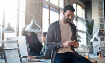 homme-assis-sur-le-coin-de-son-bureau-regarde-son-smartphone