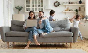 couple dans un canapé regarde son pc portable tandis que les enfants jouent derrière