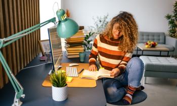 Une jeune femme étudie sur son bureau, dans son studio étudiant.