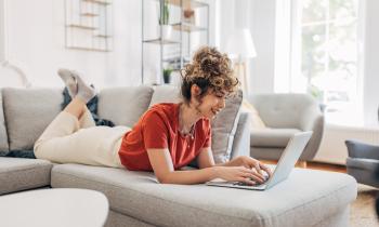 jeune femme regarde son ordinateur allongée sur son canapé