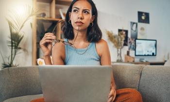 Femme qui réfléchit à son DPE, dans son canapé, l'ordinateur sur ses genoux