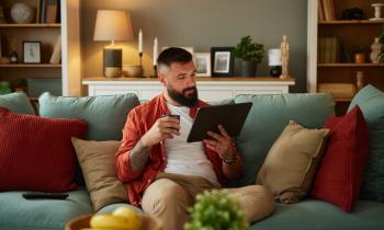 homme assis sur son canapé lit un article sur sa tablette