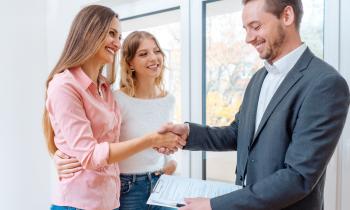 Une femme, accompagnée de sa fille, serre la main d'un agent immobilier à la fin d'une visite pour valider la signature d'un bail de location