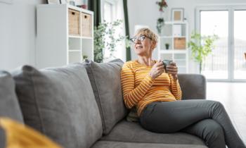 Femme buvant son café dans le salon, sur son canapé gris.