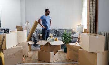 Un monsieur pensif, debout au milieu des cartons de déménagement.