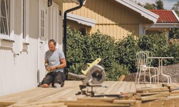 Un homme est en pleine construction d'une terrasse en bois, accolée à sa maison