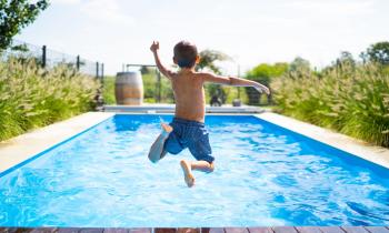 Un jeune garçon en maillot de bain saute dans une belle piscine privative bordée de plantes