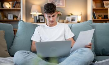Un étudiant travaille sur son ordinateur sur le canapé bleu clair du salon. 