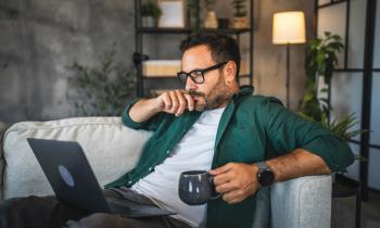 Homme assis sur son canapé, avec son mug et son ordinateur. 