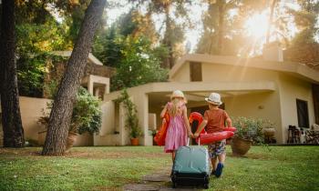 jeunes enfant traversent avec valise et bouées le jardin de la location de vacances