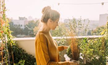 Une jeune femme portant ses cheveux relevés en chignon s'occupe de ses plantes vertes sur son balcon