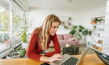 Femme avec un pull rouge sur son ordinateur dans son salon lumineux. 