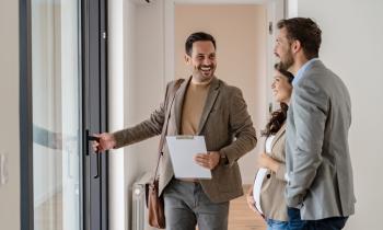 Un couple visitant un bien immobilier avec un agent en veste marron. 