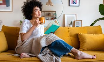Femme afro américaine souriante, avec un mug sur son canapé jaune moutarde. 