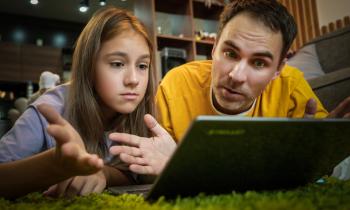 Un père et sa fille adolescente regardent un écran d'ordinateur, allongés à terre. 