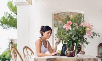 Femme recherche des conseils pour vendre sa maison l'été depuis son ordinateur sur sa terrasse