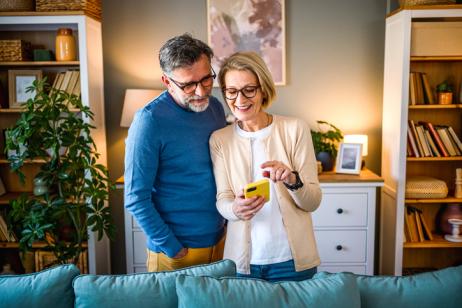 Un couple lit sur un téléphone mobile une actualité sur la taxe foncière, dans leur salon.  