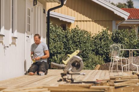 Un homme est en pleine construction d'une terrasse en bois, accolée à sa maison