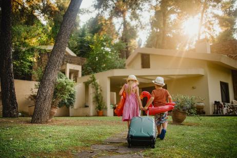 jeunes enfant traversent avec valise et bouées le jardin de la location de vacances