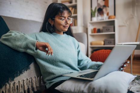 jeune femme assise près de son canapé regarde son ordinateur