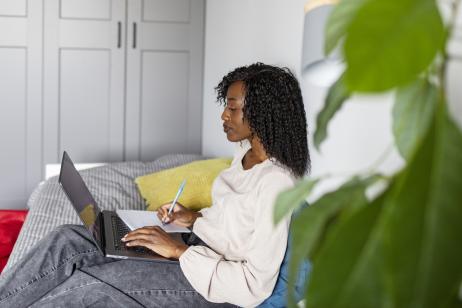 Une jeune femme fait des recherches sur son pc portable, assise sur son canapé