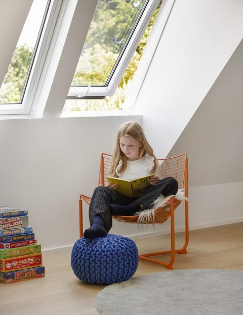 Fille qui lit dans sa chambre lumineuse grâce aux fenêtres de toit VELUX