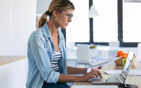 femme sur ordinateur tenant une feuille dans sa main