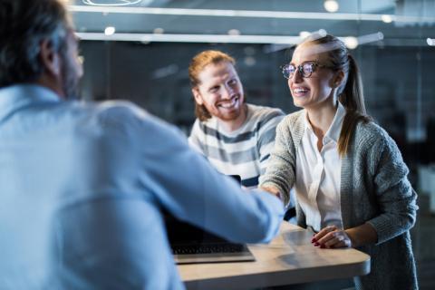 Un couple heureux serre la main d'un agent immobilier en chemise bleue