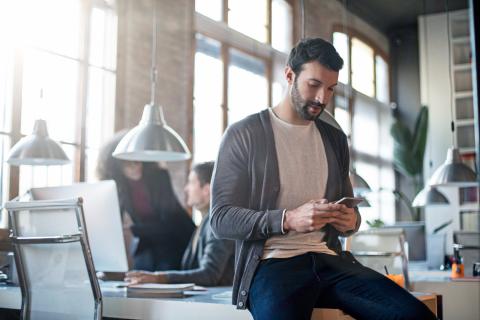 homme-assis-sur-le-coin-de-son-bureau-regarde-son-smartphone