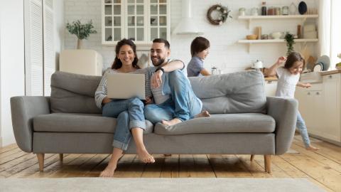 couple dans un canapé regarde son pc portable tandis que les enfants jouent derrière