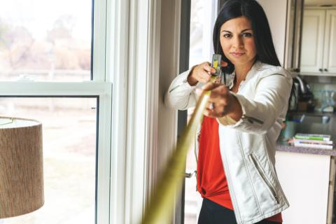 Femme mesurant une maison avec un mètre jaune. 