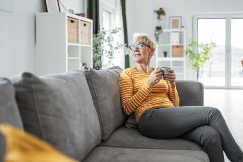 Femme buvant son café dans le salon, sur son canapé gris.