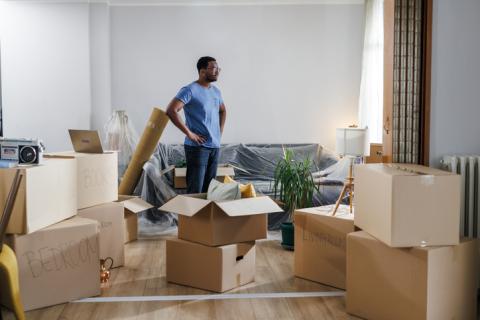 Un monsieur pensif, debout au milieu des cartons de déménagement. 